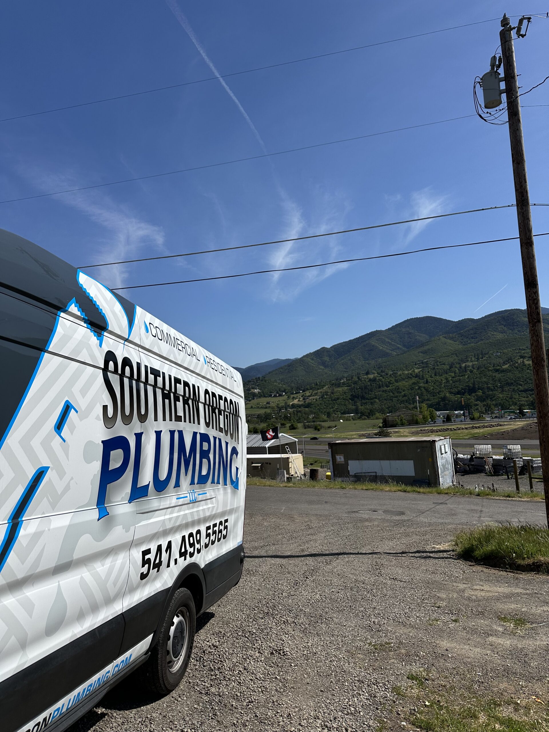 A white van with SOUTHERN OREGON PLUMBING and a phone number on the side is parked on a gravel lot.